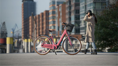 Una mujer corre por una ciudad hacia una bicicleta eléctrica rosa Cube Ella Hybrid.