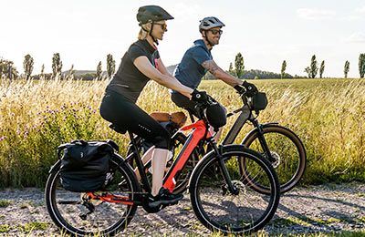 Se ve a una pareja circulando en bicicletas eléctricas por un camino de grava. Al fondo se ve hierba alta.