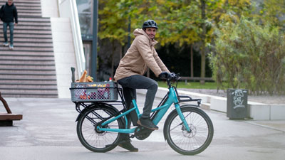 Un ciclista recorre el centro de la ciudad con su bicicleta azul Cube Longtail. Lleva una caja con comida en el portaequipajes.