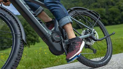 Se muestra un primer plano de una bicicleta híbrida todoterreno Cube Reaction gris. Se observa con más detalle el pedalier y el bloque del motor de la bicicleta eléctrica durante la marcha.