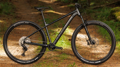 Se ve una bicicleta de montaña Cube negra parada en un camino forestal.