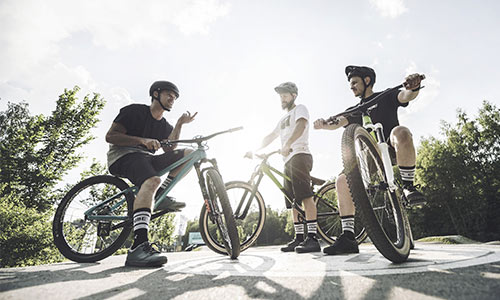 Tres ciclistas de estilo libre están junto a sus bicicletas charlando en un día soleado.