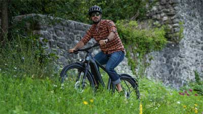 Un ciclista recorre un prado con su bicicleta de montaña, con un muro de piedra al fondo.
