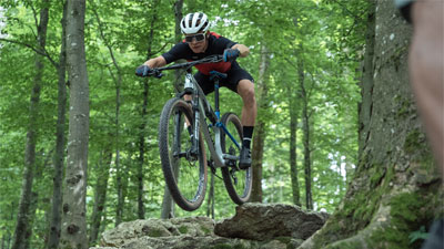 Un ciclista va por el bosque y salta de una piedra.