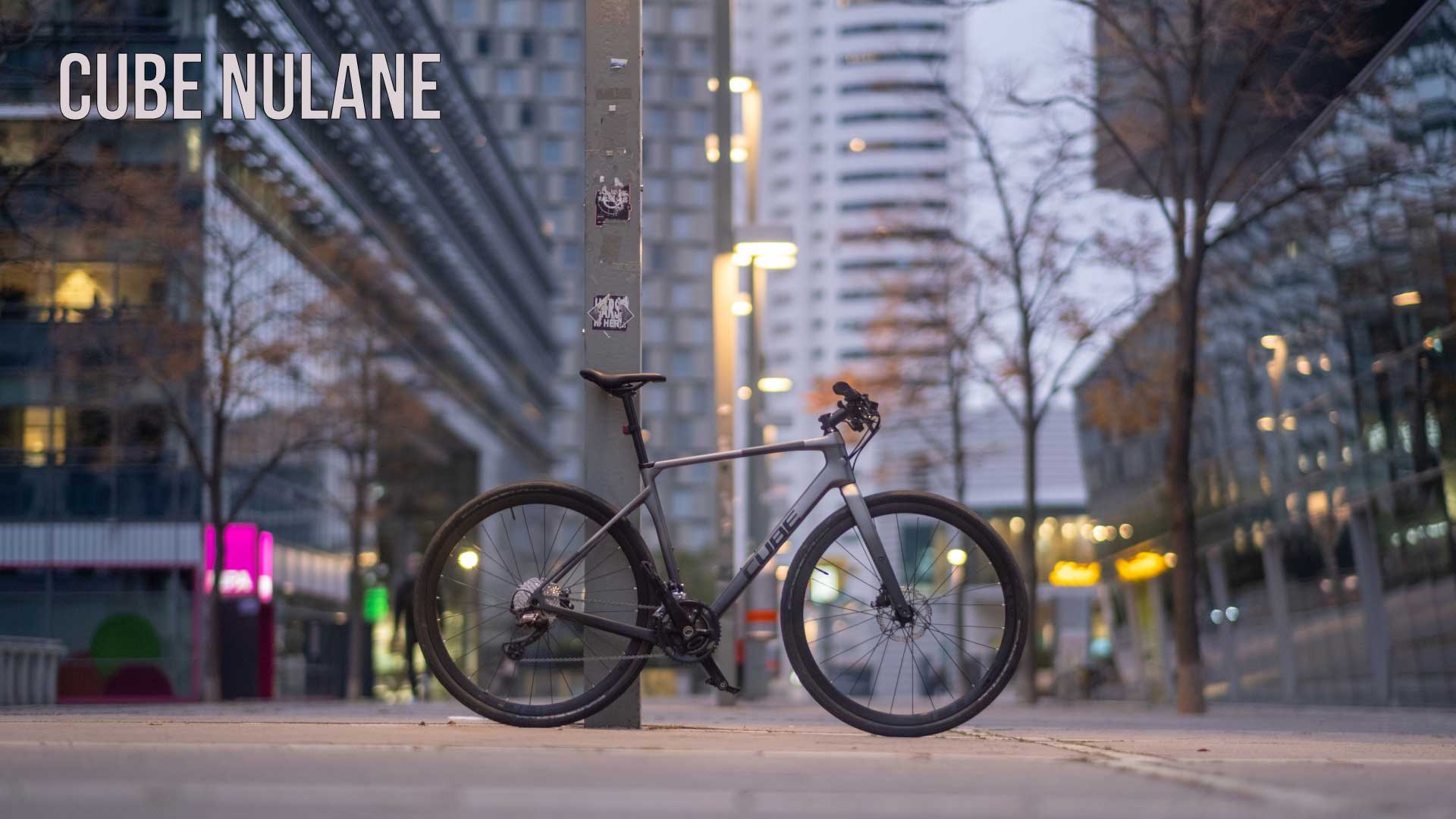 Cartel con la inscripción Cube Nulane. Una bicicleta Cube Nulane apoyada contra una columna en el centro de la ciudad.