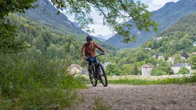 Un ciclista recorre un camino de grava con su bicicleta de montaña, con un paisaje montañoso al fondo.
