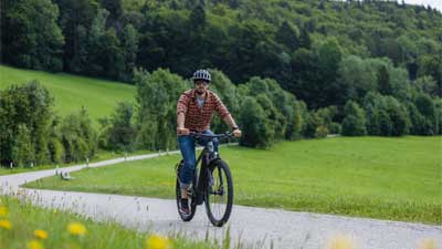 Un ciclista recorre con su bicicleta de montaña un carril bici asfaltado, con un paisaje rural al fondo.