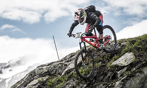 Ciclista de descenso con casco integral bajando por una montaña rocosa.
