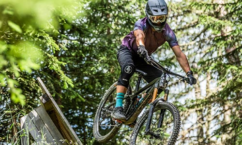 Ciclista con casco integral circulando por el bosque en una bicicleta de montaña con suspensión total.
