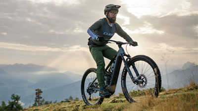 Se ve a un hombre montado en una bicicleta eléctrica Cube Stereo Hybrid gris circulando por un sendero.