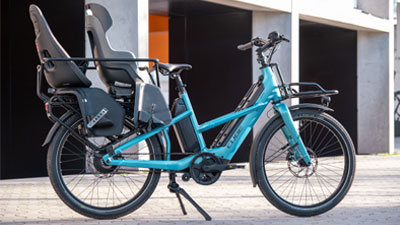 Se puede ver una bicicleta eléctrica de carga Cube Longtail Hybrid azul con dos asientos infantiles equipados.