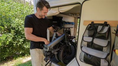 Un hombre coloca su bicicleta plegable gris en su autocaravana abierta.