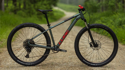 Se ve una bicicleta de montaña Cube gris con detalles rojos en un camino de grava.