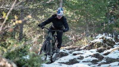 Una ciclista recorre con su bicicleta de montaña un bosque accidentado, en parte aún cubierto de nieve.