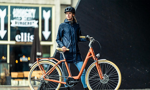 Una mujer está de pie detrás de su bicicleta urbana naranja, en el centro de la ciudad.